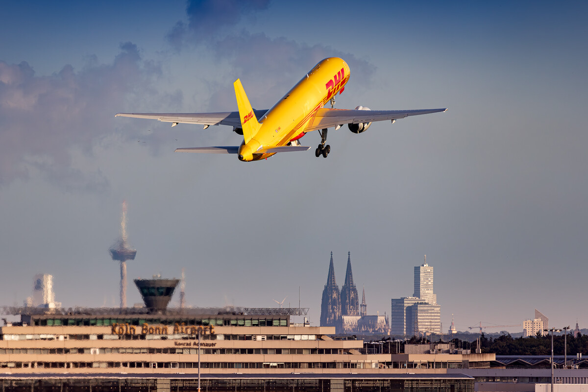 DHL Boeing 757-200 Freighter "G-BMRI" taking off from runway 31R at Köln Bonn Airport on a bright and sunny morning right in front of the airport buildings and the Cologne Cathedral, May 2024.